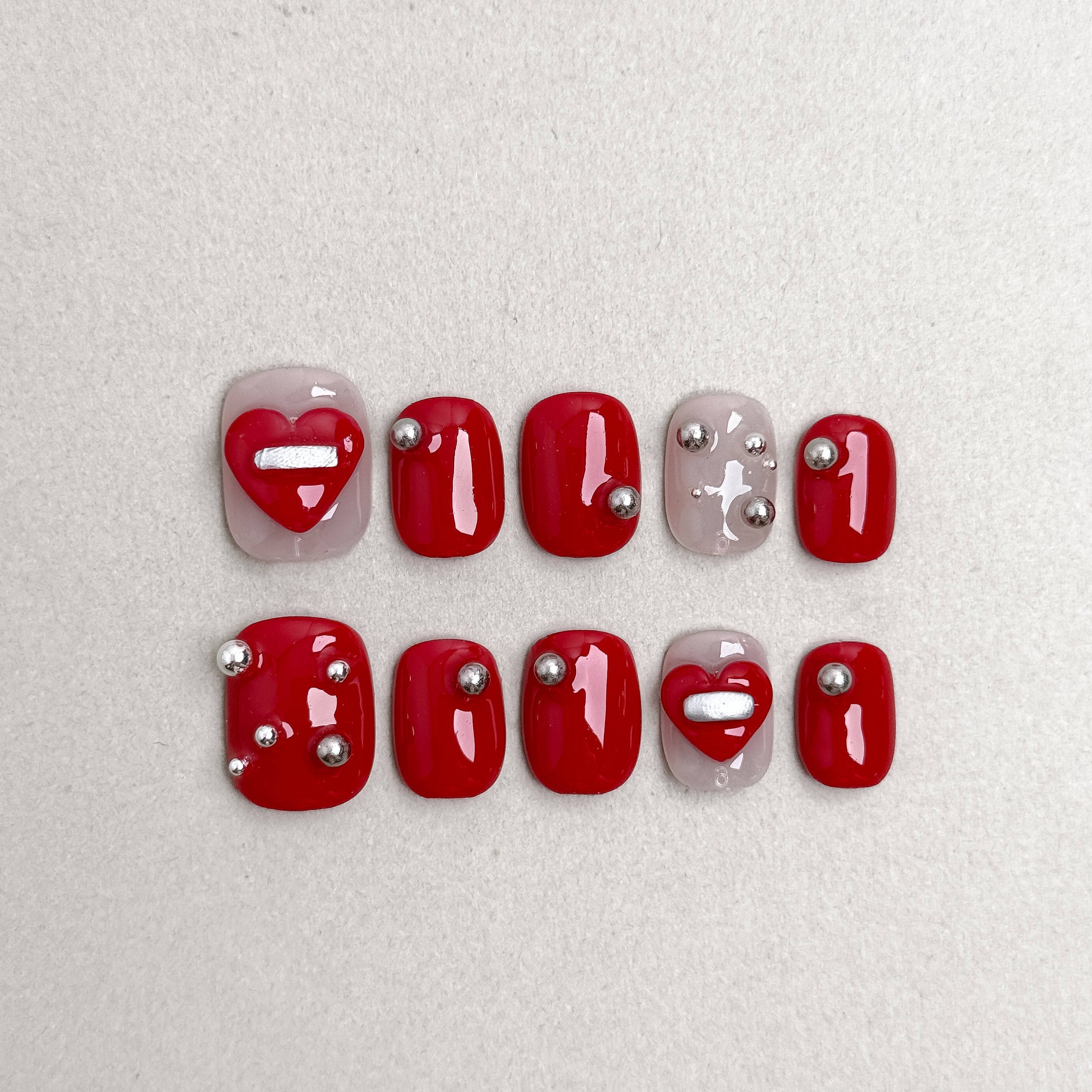 Set of reusable press-on nails in glossy red with silver heart accents, MIBLAB Affair collection Geneva.