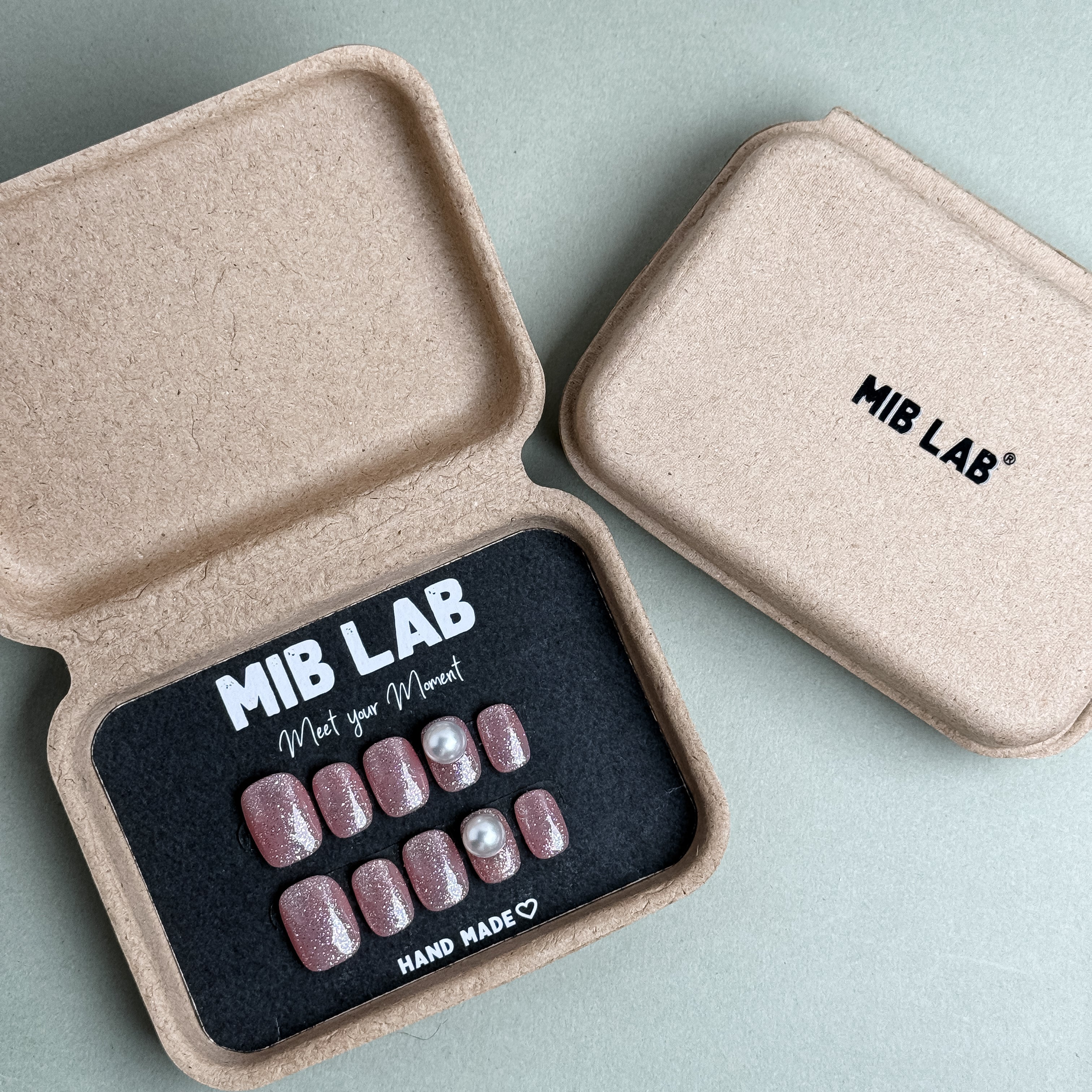 MIBLAB Briller press-on nail set in nude pink glitter finish with elegant pearl details, packaged for boutique display in Geneva.