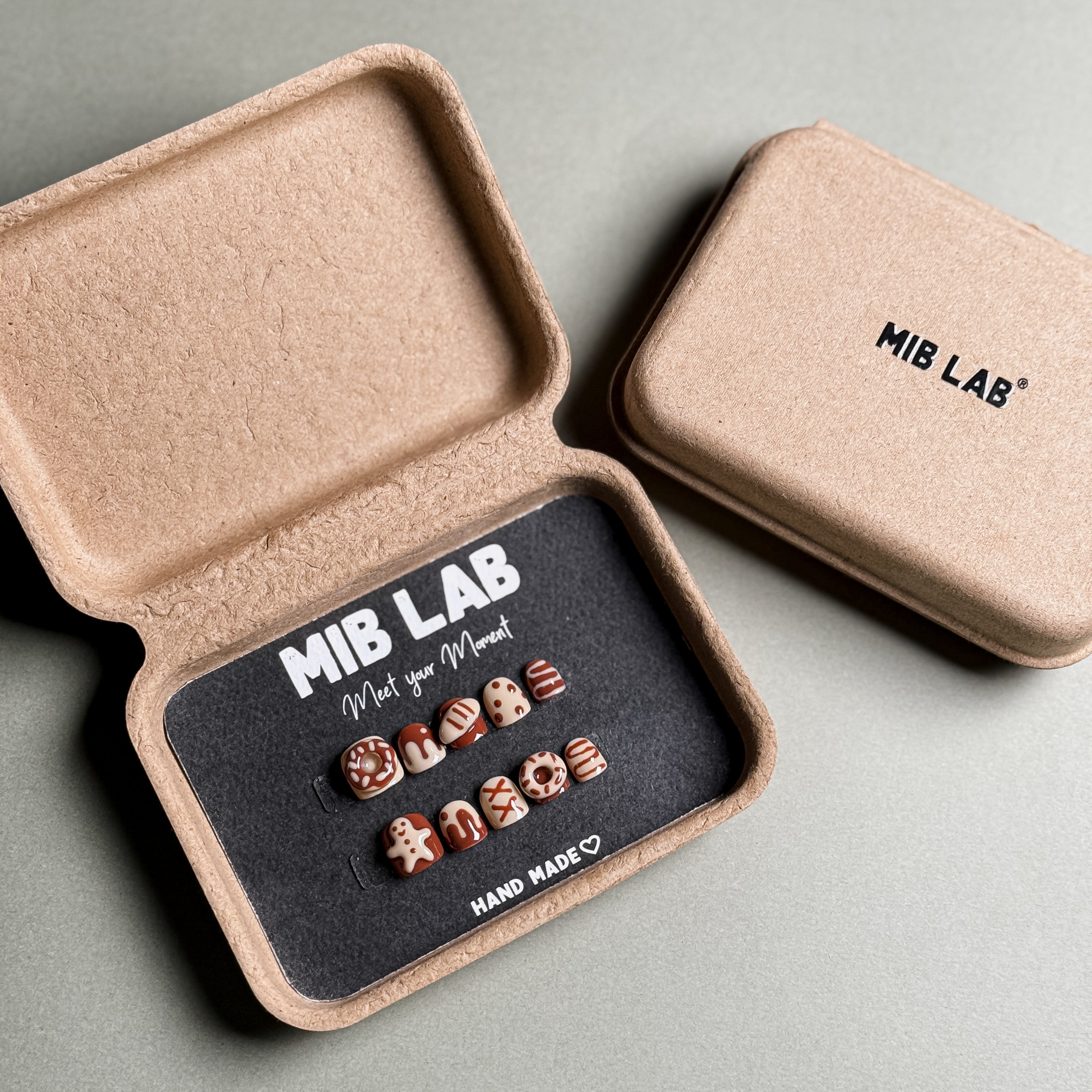 A set of Handmade press on nails with playful donut and sprinkle designs, presented in eco-friendly packaging. These Custom press on nails offer a fun and whimsical look, perfect for Everyday nails with a unique touch. The box, labeled "MIB LAB" and "Meet Your Moment", highlights the brand's dedication to creating personalized Nail art designs. Ideal for those seeking Reusable fake nails that combine style and creativity.