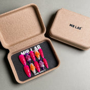 A set of Handmade press on nails with vibrant pink hues and floral accents, presented in eco-friendly packaging. These Custom press on nails offer a bold and feminine look, perfect for Party nails or special occasions. The box, labeled "MIB LAB" and "Meet Your Moment", highlights the brand's dedication to creating memorable Nail art designs. Ideal for those seeking Reusable fake nails that combine style and sustainability.