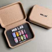 A set of Handmade press on nails with a variety of colorful and detailed designs, presented in eco-friendly packaging. These Custom press on nails offer a range of styles, perfect for Everyday nails with a unique touch. The box, labeled "MIB LAB" and "Meet Your Moment", highlights the brand's dedication to creating personalized Nail art designs. Ideal for those seeking Reusable fake nails that combine style and sustainability.