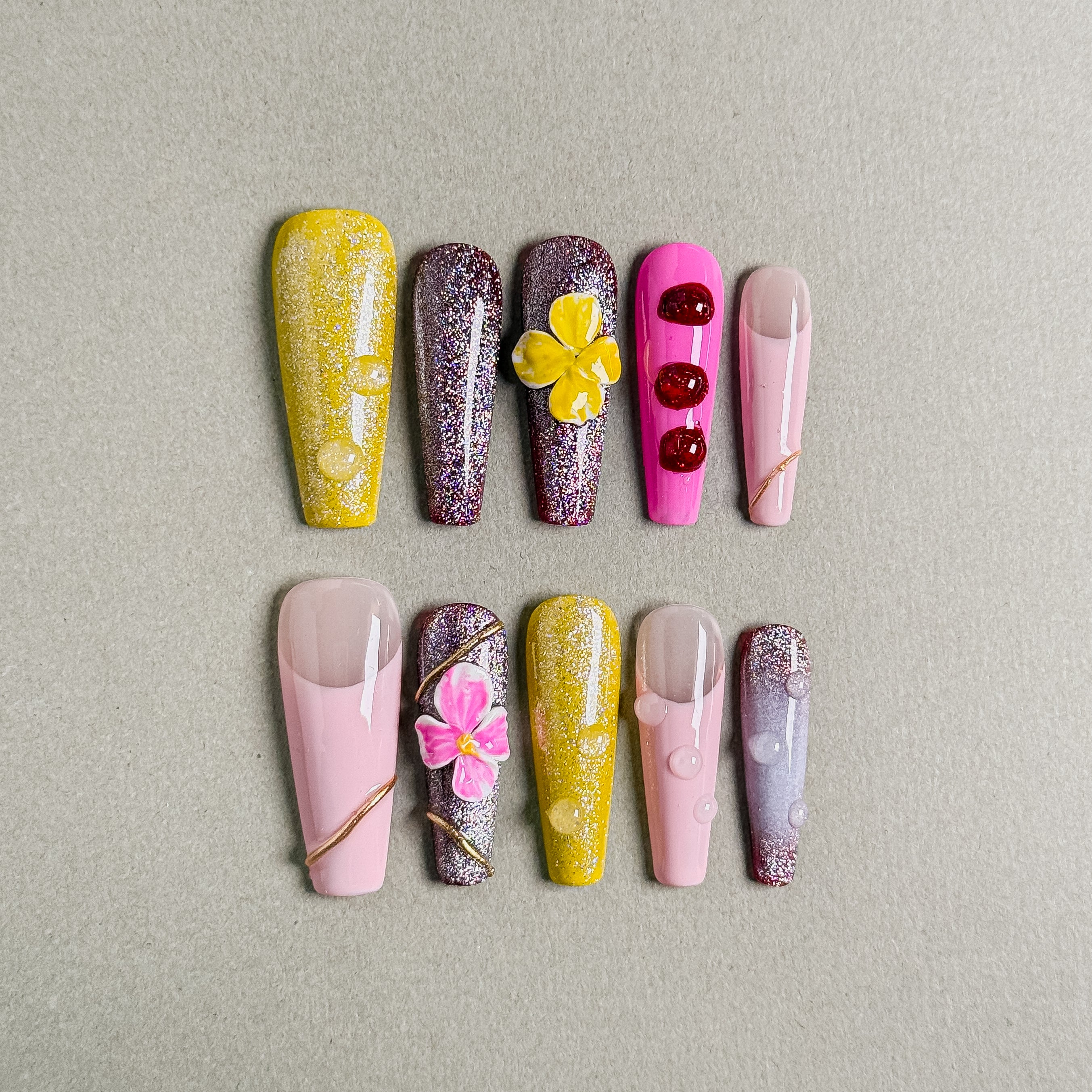 A set of "Waikiki" stiletto - shaped press - on nails featuring a colorful array of tropical designs, including flowers, glitter, and unique patterns in hues like yellow, pink, and purple, ideal for adding a lively, beachy touch to party nail styles.
