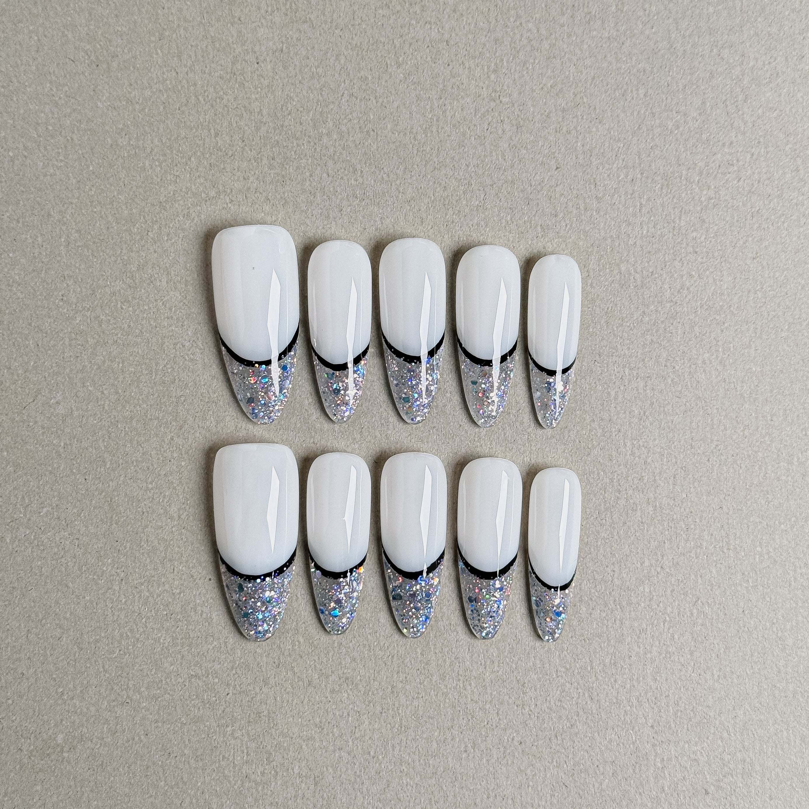 A set of "Beam" long press - on nails with white bases and sparkly silver - glitter tips, separated by a thin black line, perfect for creating a glamorous and stylish nail look for special events.
