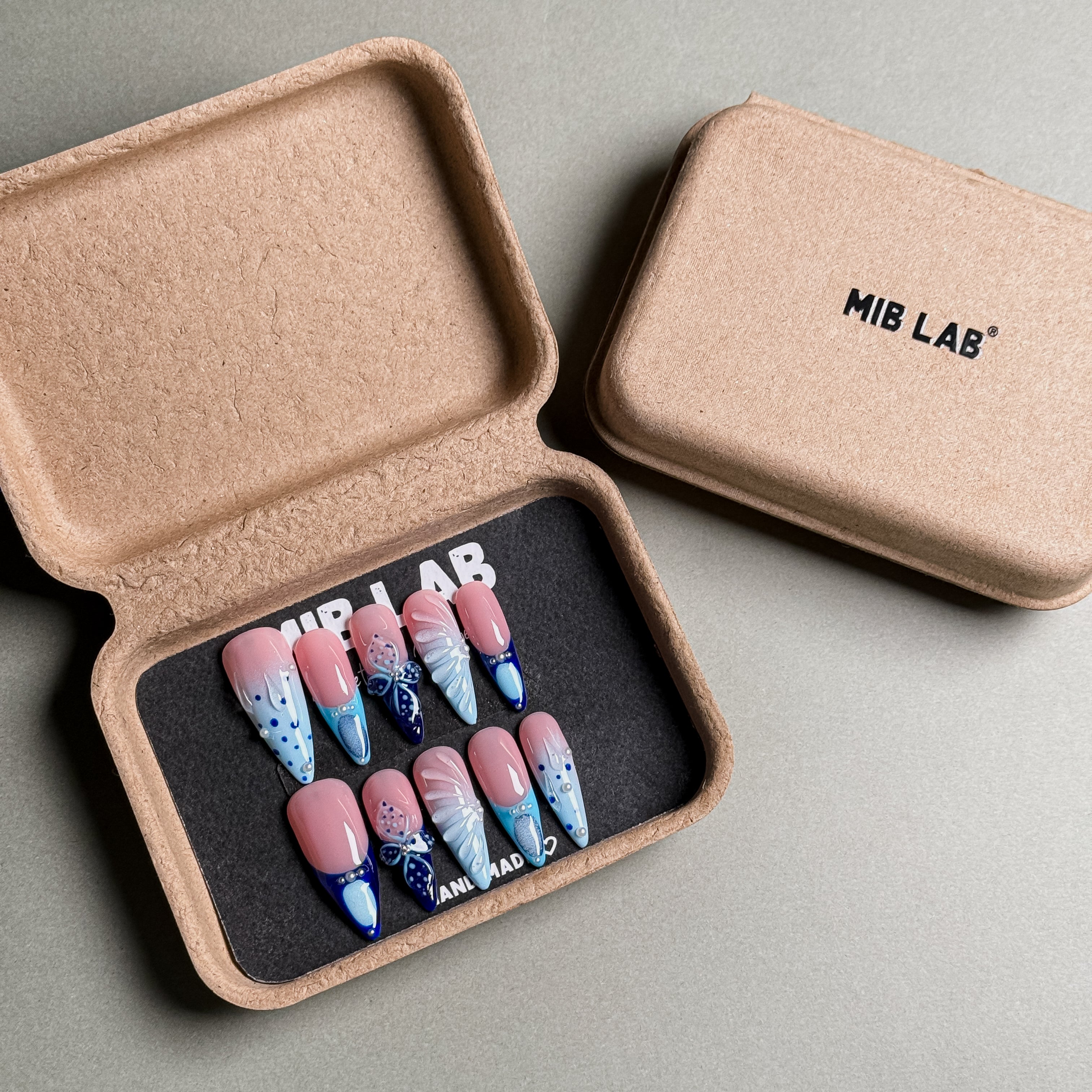 A set of Handmade press on nails with a delicate blue and white design, featuring butterfly and dot patterns, presented in eco-friendly packaging. These Custom press on nails offer a whimsical and elegant look, perfect for Everyday nails with a unique touch. The box, labeled "MIB LAB" and "Meet Your Moment", highlights the brand's dedication to creating personalized Nail art designs. Ideal for those seeking Reusable fake nails that combine style and sustainability.