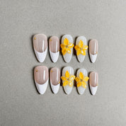 A set of "White Tea" coffin - shaped press - on nails featuring a soft color palette with white and light pink bases, decorated with vibrant yellow flowers and small gold accents, ideal for creating a romantic and refined nail look for weddings.
