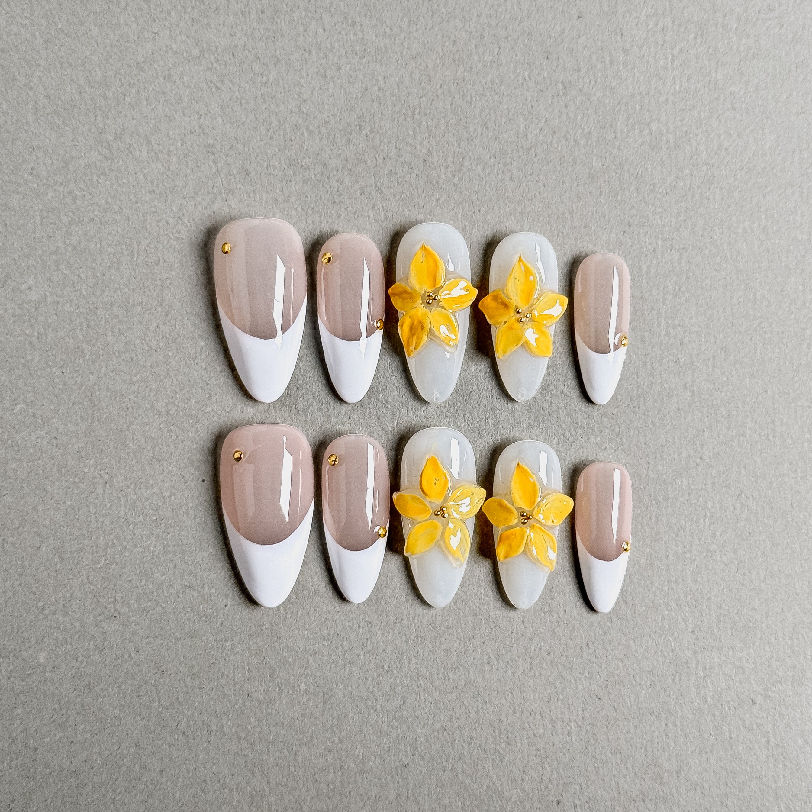 A set of "White Tea" coffin - shaped press - on nails featuring a soft color palette with white and light pink bases, decorated with vibrant yellow flowers and small gold accents, ideal for creating a romantic and refined nail look for weddings.

