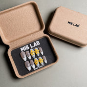 A set of Handmade press on nails with a classic French tip design and delicate yellow flower accents, presented in eco-friendly packaging. These French tip nails offer a timeless and elegant look, perfect for Wedding nails or everyday wear. The box, labeled "MIB LAB" and "Meet Your Moment", highlights the brand's dedication to creating memorable Nail art designs. Ideal for those seeking Reusable fake nails that combine style and sophistication.