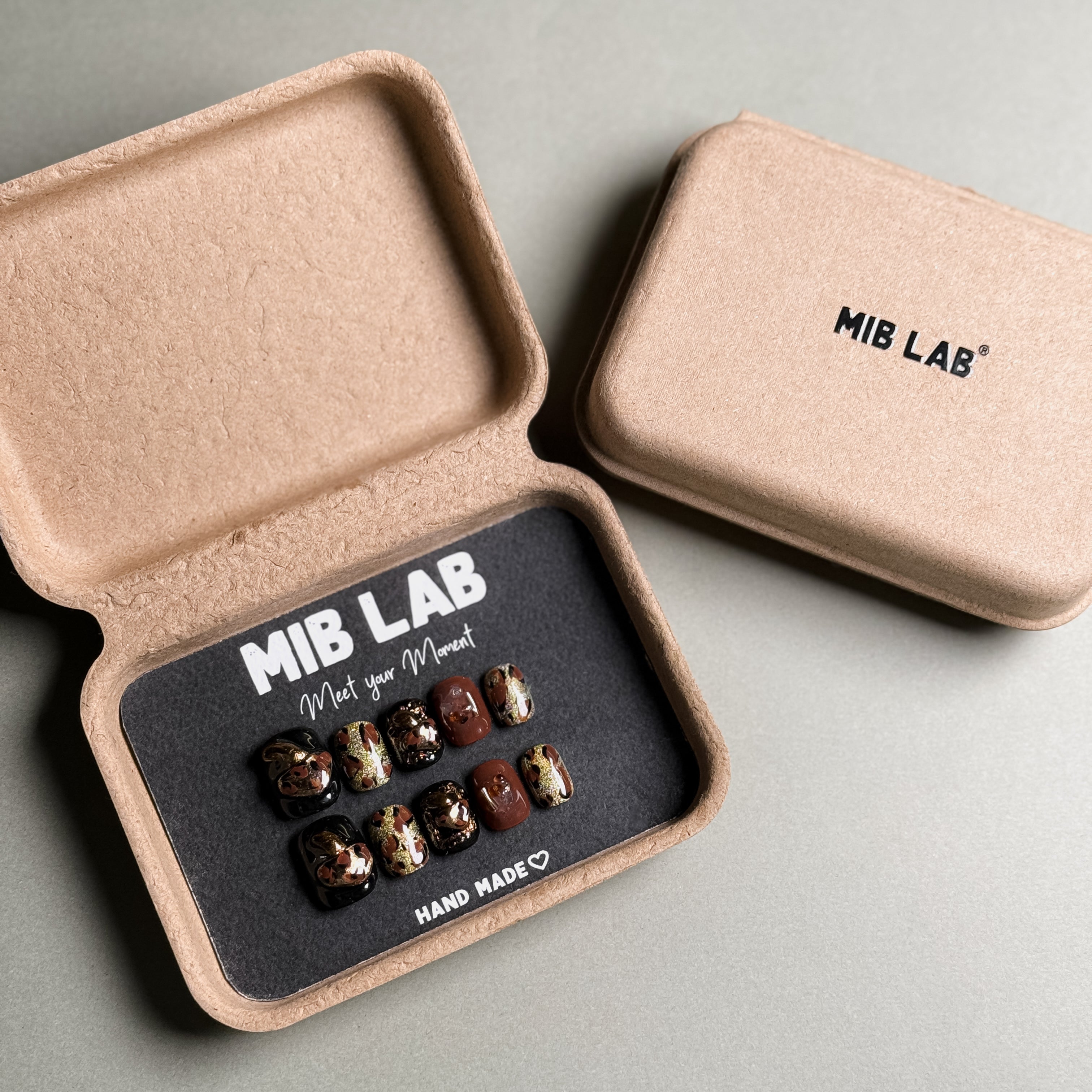 A set of Handmade press on nails with a bold leopard print and gold accents, presented in eco-friendly packaging. These Custom press on nails offer a stylish and edgy look, perfect for Party nails or everyday wear. The box, labeled "MIB LAB" and "Meet Your Moment", highlights the brand's dedication to creating memorable Nail art designs. Ideal for those seeking Reusable fake nails that make a statement.