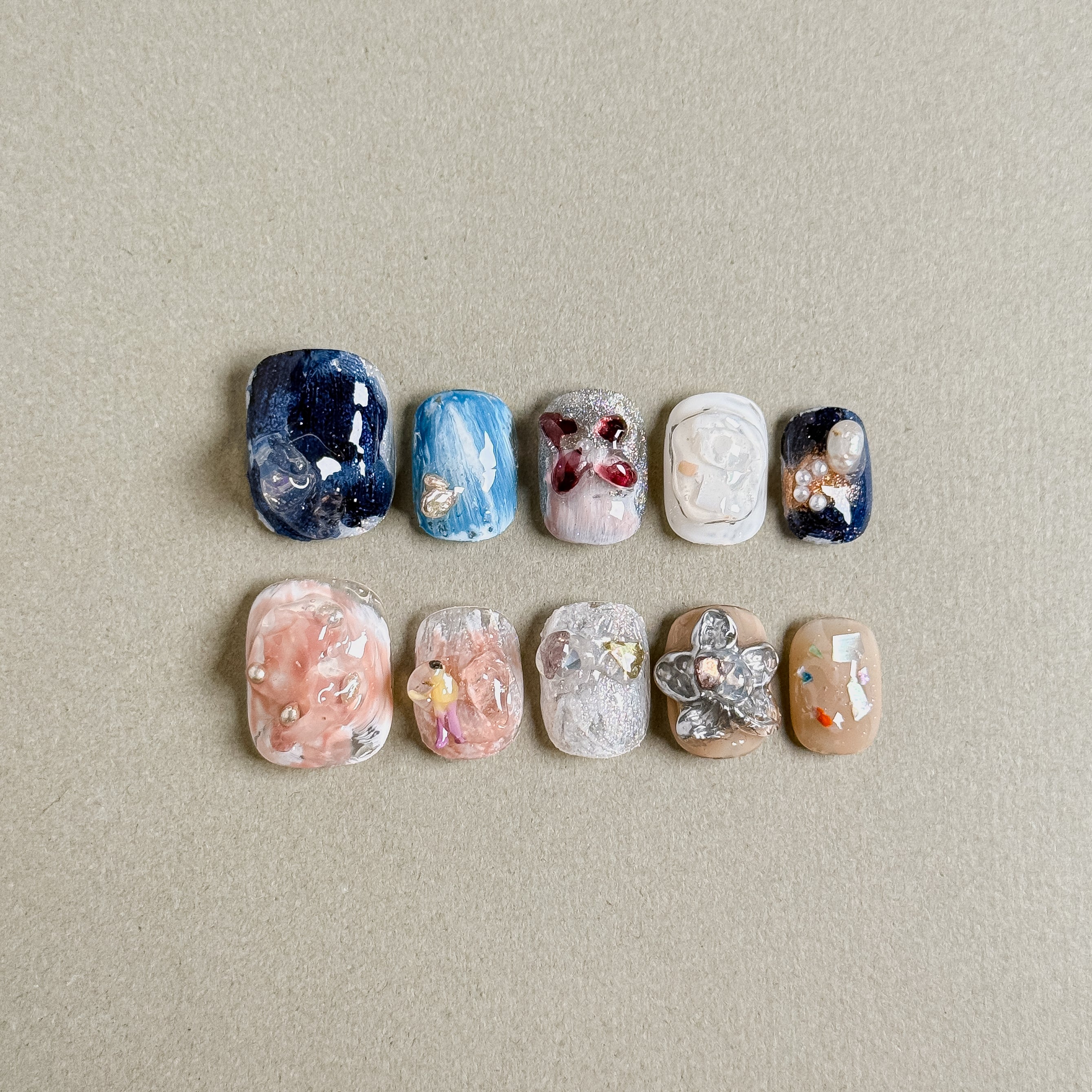 A set of "Faded" press - on nails showcasing a range of colors and intricate designs, including floral motifs, glitter, and stone - like textures, perfect for making a statement at parties with unique nail art.
