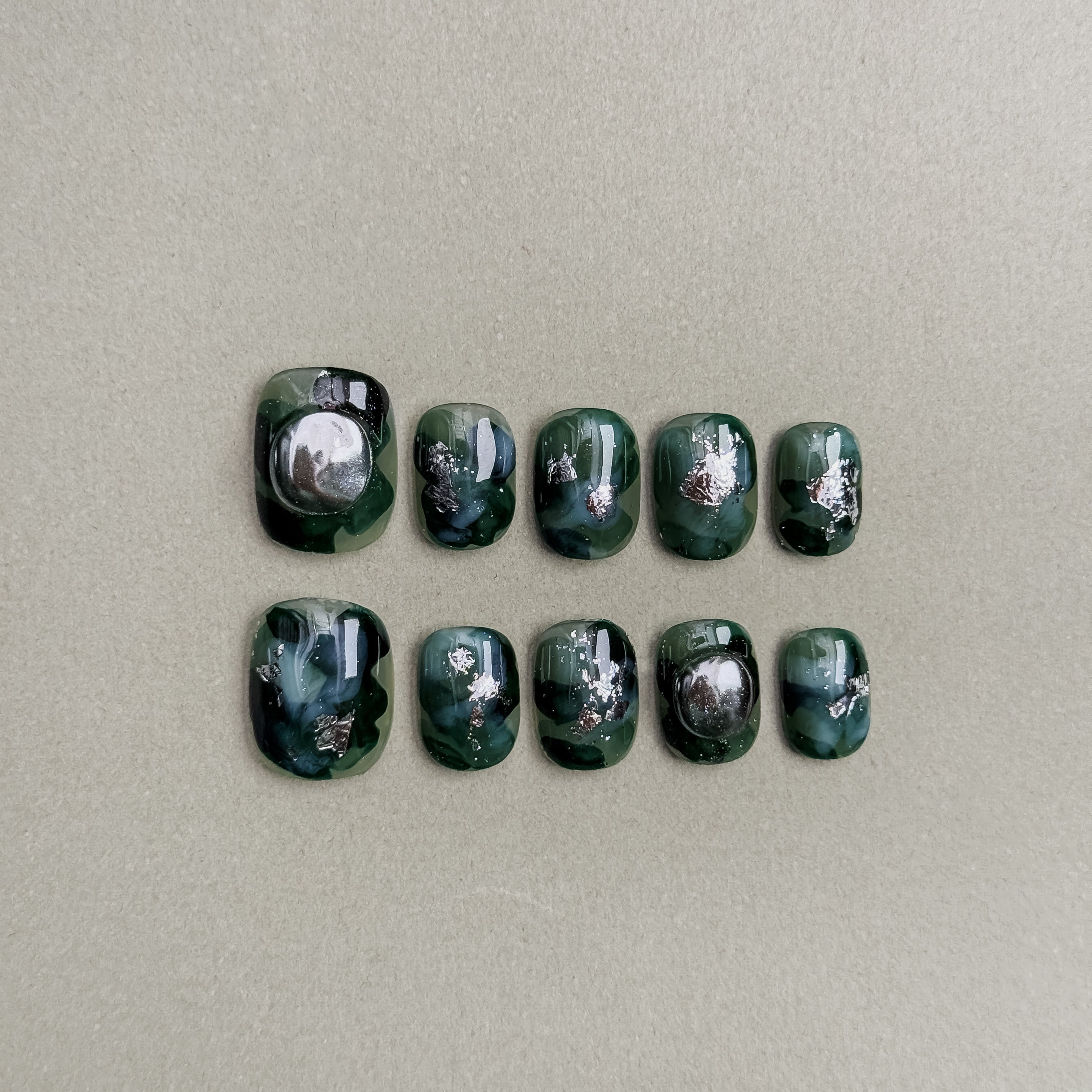 A set of "Symphony" press - on nails in rich, dark green hues, adorned with intricate silver and black patterns and circular embellishments, perfect for adding a touch of sophistication to wedding nail styles.
