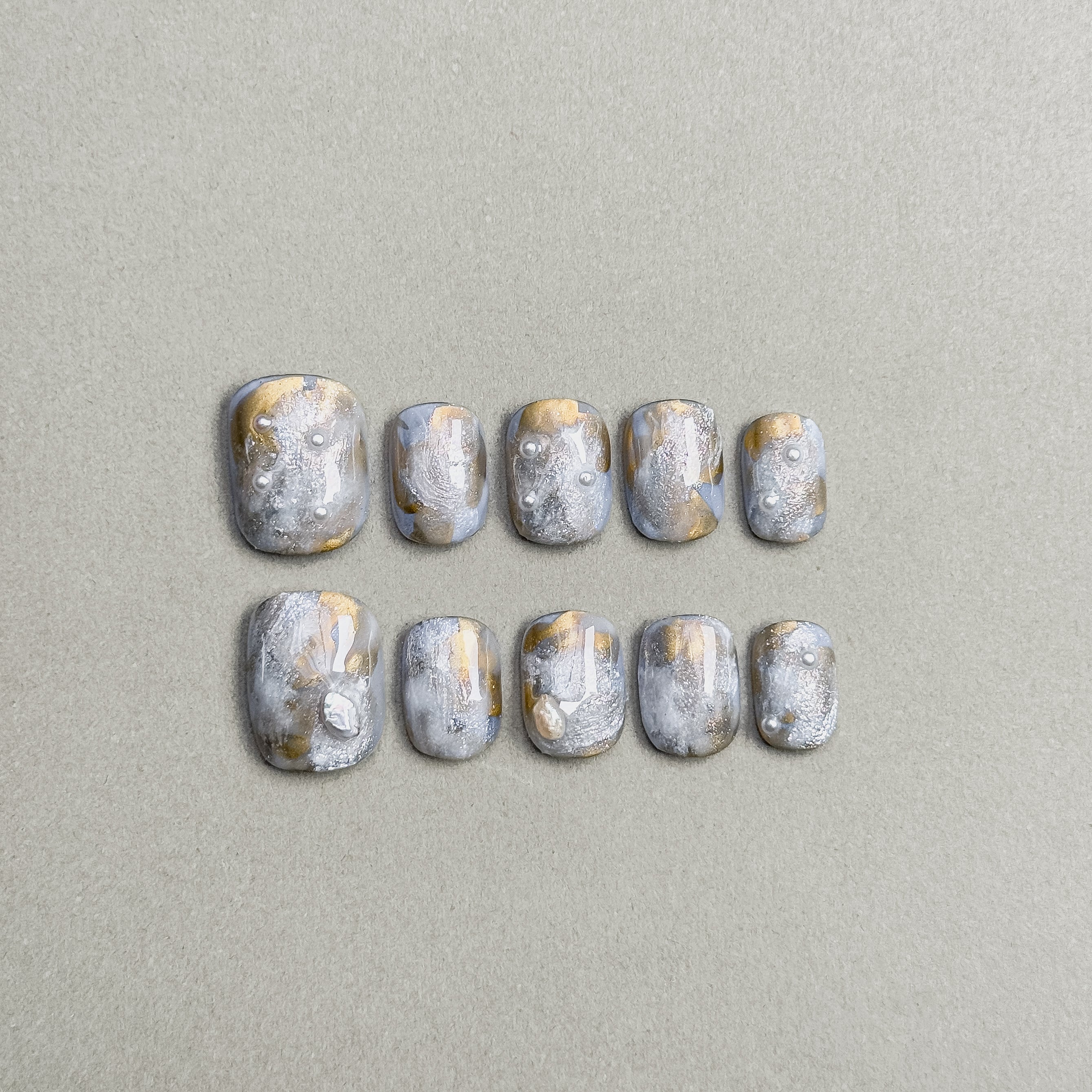 A set of "Mirage" press - on nails with a dreamy blend of gray and gold tones, featuring unique textures and patterns, ideal for creating an other - worldly and eye - catching nail look for parties.
