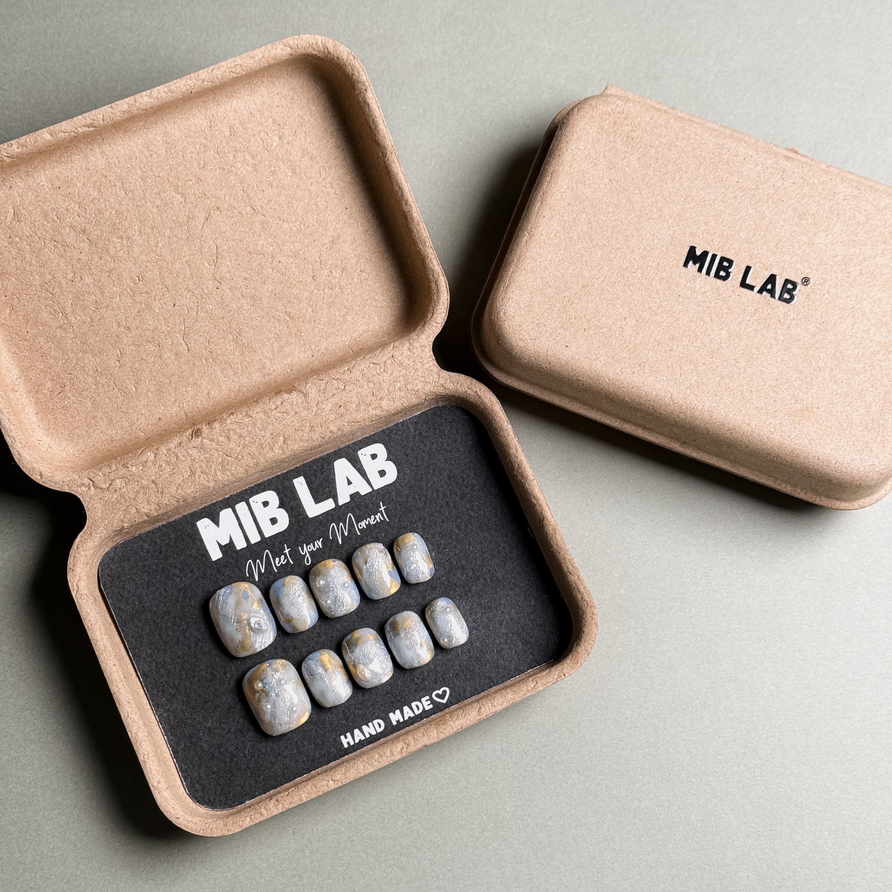 A set of Handmade press on nails with a minimalist marble design, presented in eco-friendly packaging. These Minimalist nails offer a clean and sophisticated look, perfect for Everyday nails and professional settings. The box, labeled "MIB LAB" and "Meet Your Moment", highlights the brand's dedication to creating timeless Nail art designs. Ideal for those seeking Reusable fake nails that are both stylish and sustainable.