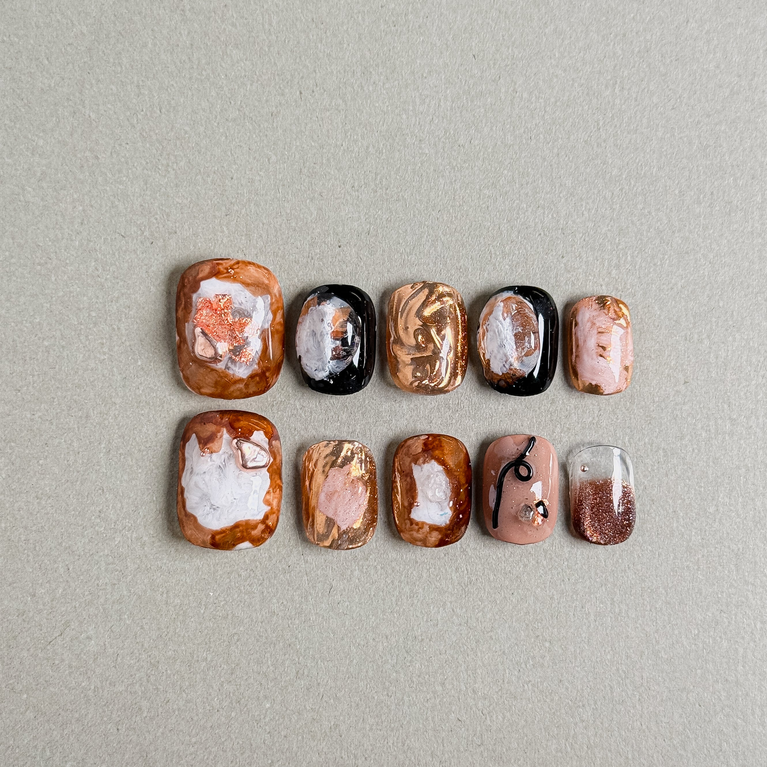 A set of "Iced Toffee" press - on nails featuring a palette of warm, earthy tones with intricate patterns and metallic accents, perfect for adding an elegant and unique touch to wedding - day nail looks.
