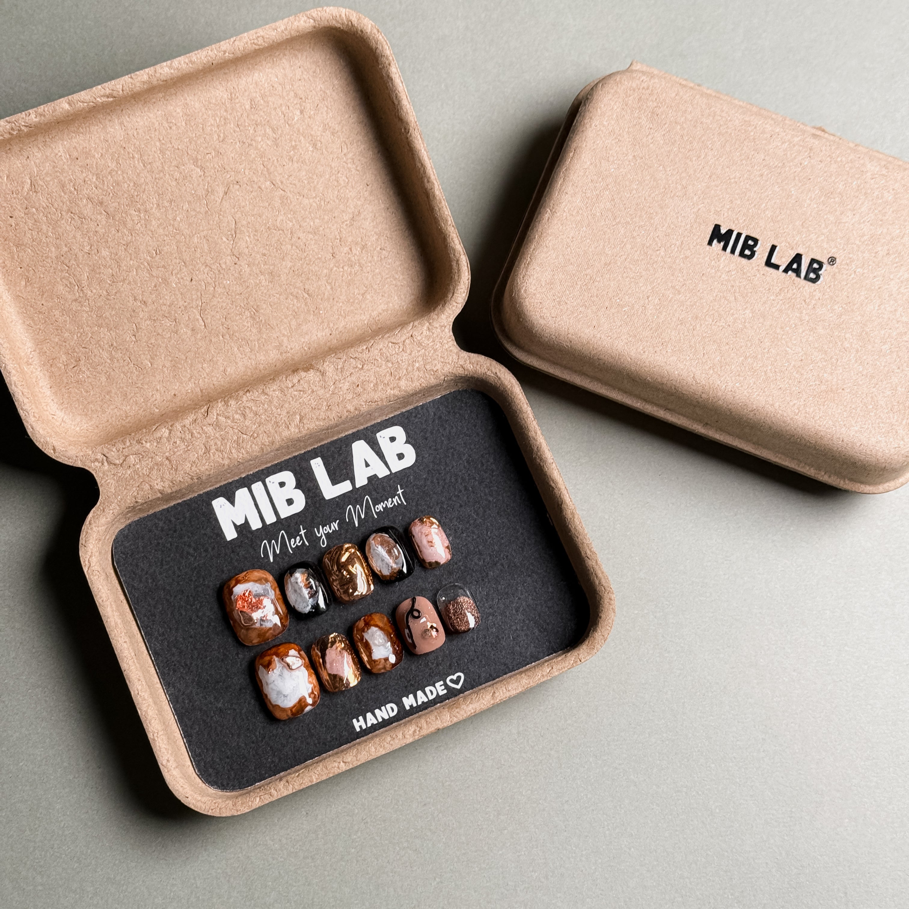 A set of Handmade press on nails with unique tortoise shell and gold foil designs, presented in eco-friendly packaging. These Custom press on nails offer a sophisticated and artistic look, ideal for Everyday nails with a touch of luxury. The box, labeled "MIB LAB" and "Meet Your Moment", emphasizes the brand's commitment to creating personalized Nail art designs. Perfect for those seeking Luxury press on nails that stand out.