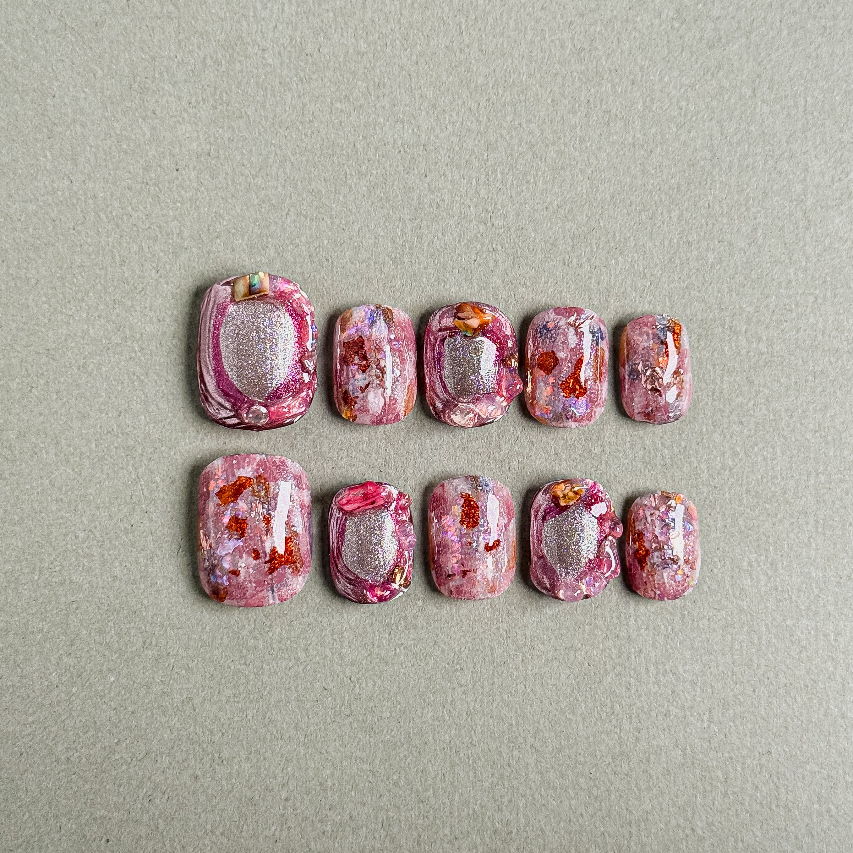 A set of "Serenade" press - on nails with a striking blend of pink hues, glitter, and artistic splashes, creating a one - of - a - kind look for making a statement at parties.
