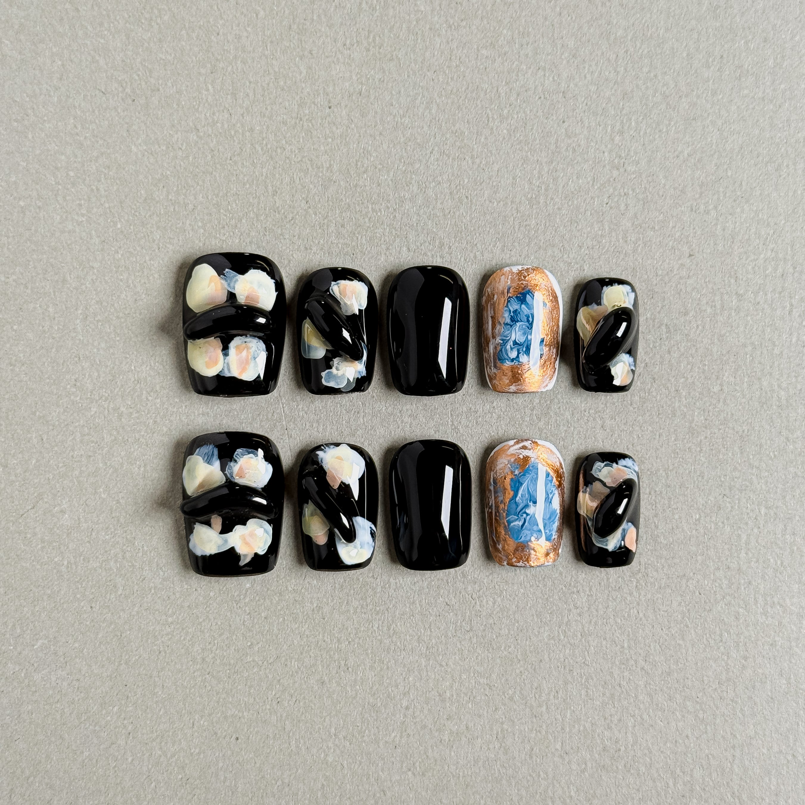 Black short press-on fake nails with abstract color patterns (gold, blue, pink) and 3D black decorations, handmade custom nails.