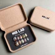 A set of handcrafted Handmade press on nails displayed in a sustainable packaging box, featuring a variety of unique designs. This Nail art kit showcases Custom press on nails with intricate details and embellishments. Ideal for Nail art designs and those seeking Luxury press on nails for special occasions. The box is labeled "MIB LAB" and "Meet Your Moment", emphasizing the brand's commitment to quality and individuality.