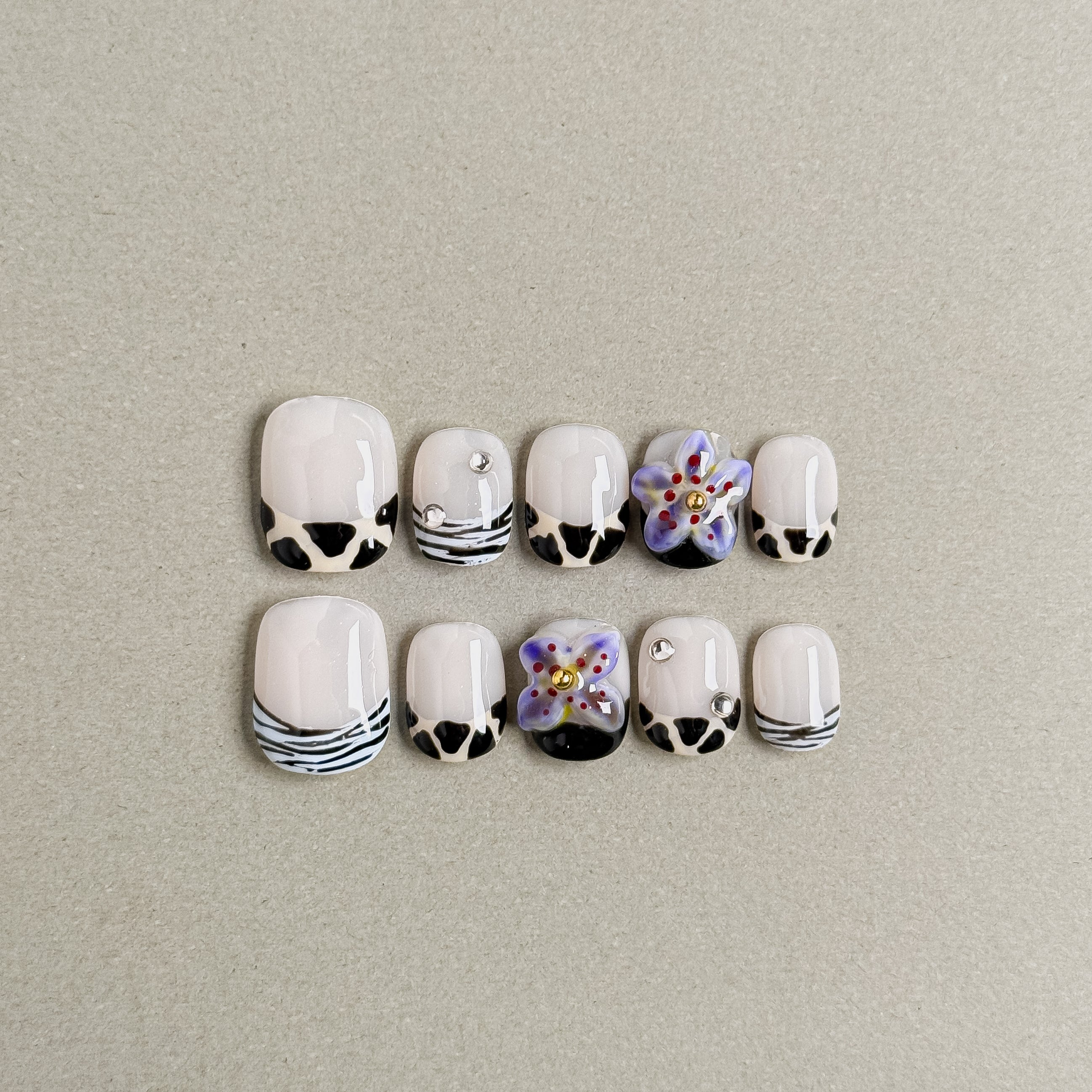 A set of "Wild Summer" press - on nails with a mix of white bases adorned with black patterns, delicate flowers, and small rhinestones, ideal for adding a lively touch to holiday party nail looks.

