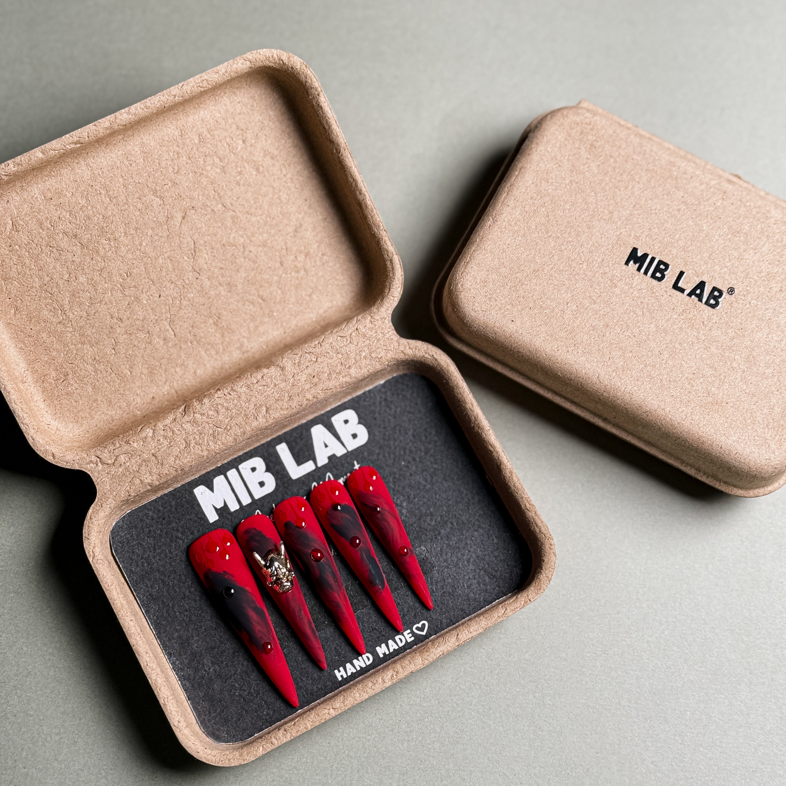 MIBLAB's Stiletto nails set with red and black design, featuring a gold accent. Packaged in an eco-friendly box with "MIB LAB" branding. Ideal for party nails or holiday nails, showcasing luxury press on nails. Offers handmade press on nails look with unique nail art designs.