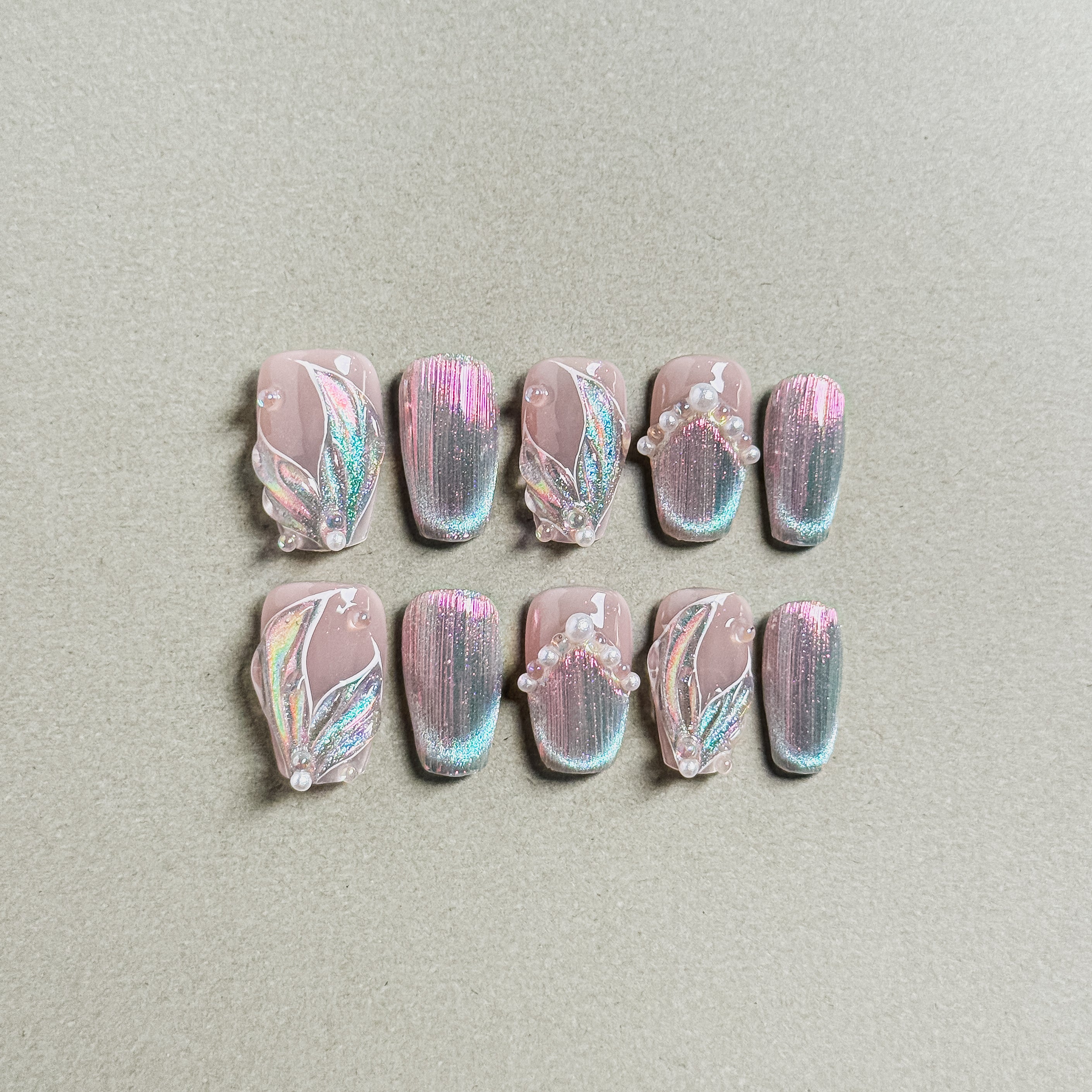 A set of "Aqua" press - on nails with a soft pink base, adorned with iridescent glitter, intricate designs, and small pearl accents, perfect for adding a touch of elegance to wedding or party nail looks.