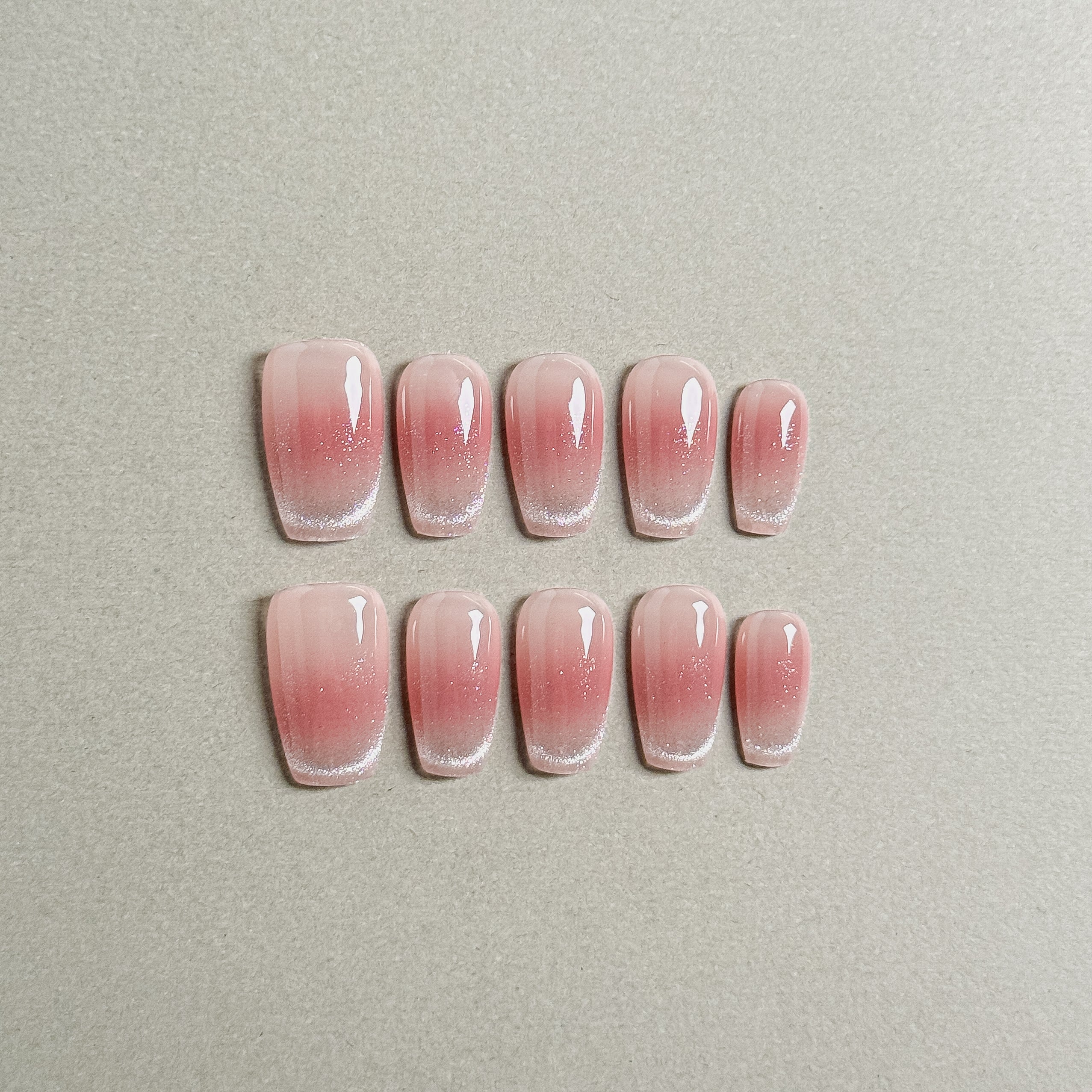 A set of "Solar" press - on nails showcasing a soft pink gradient with fine glitter accents, creating a radiant and natural - looking effect, perfect for festive holiday nail designs.