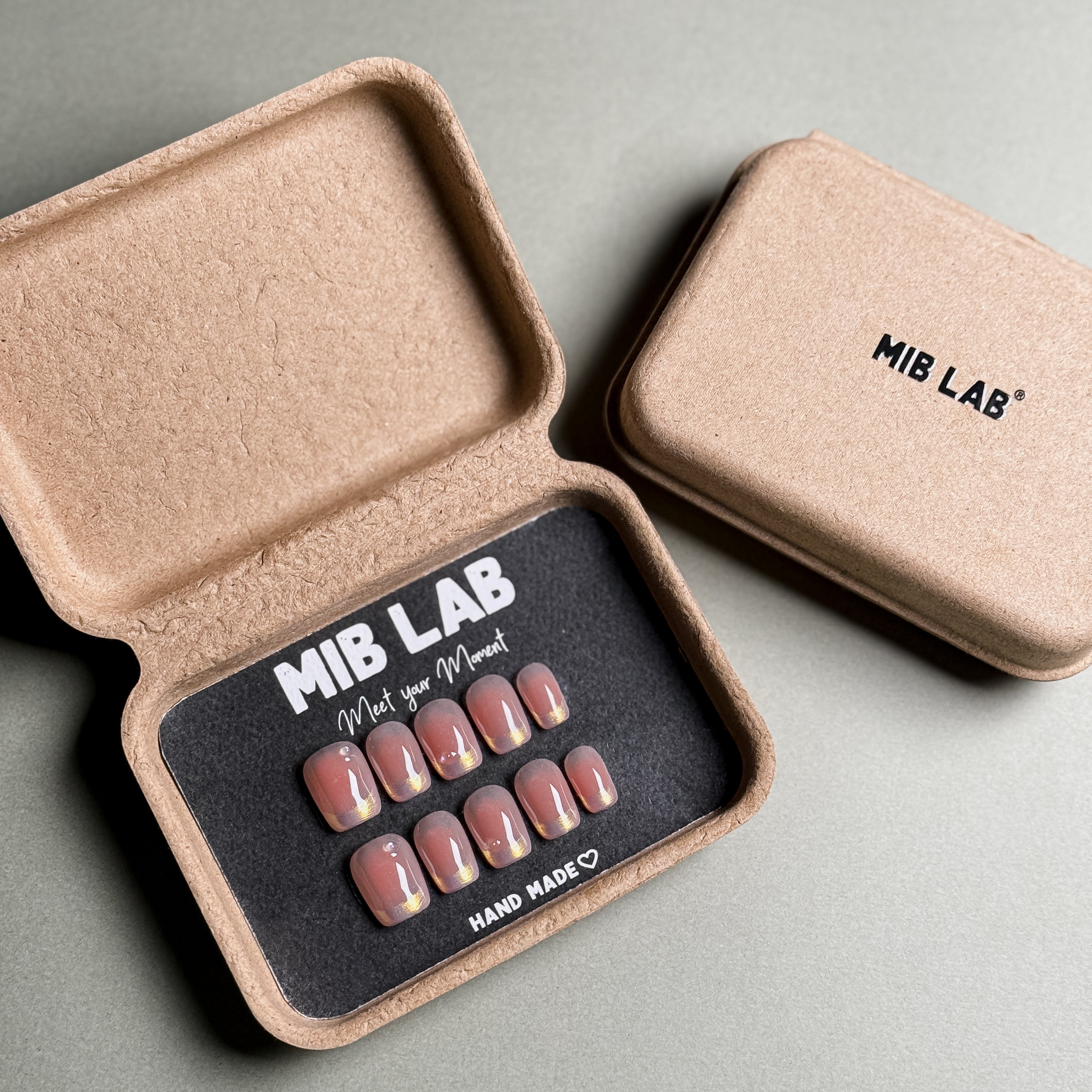 MIBLAB's nude shimmer press-on nails set, showcasing a pearlescent finish in a recycled paper box. Features brand name "MIB LAB" and "Meet your Moment" slogan. Ideal for everyday nails or minimalist nails, offering a natural looking nails effect. This luxury press-on nails set provides professional nail art at home.