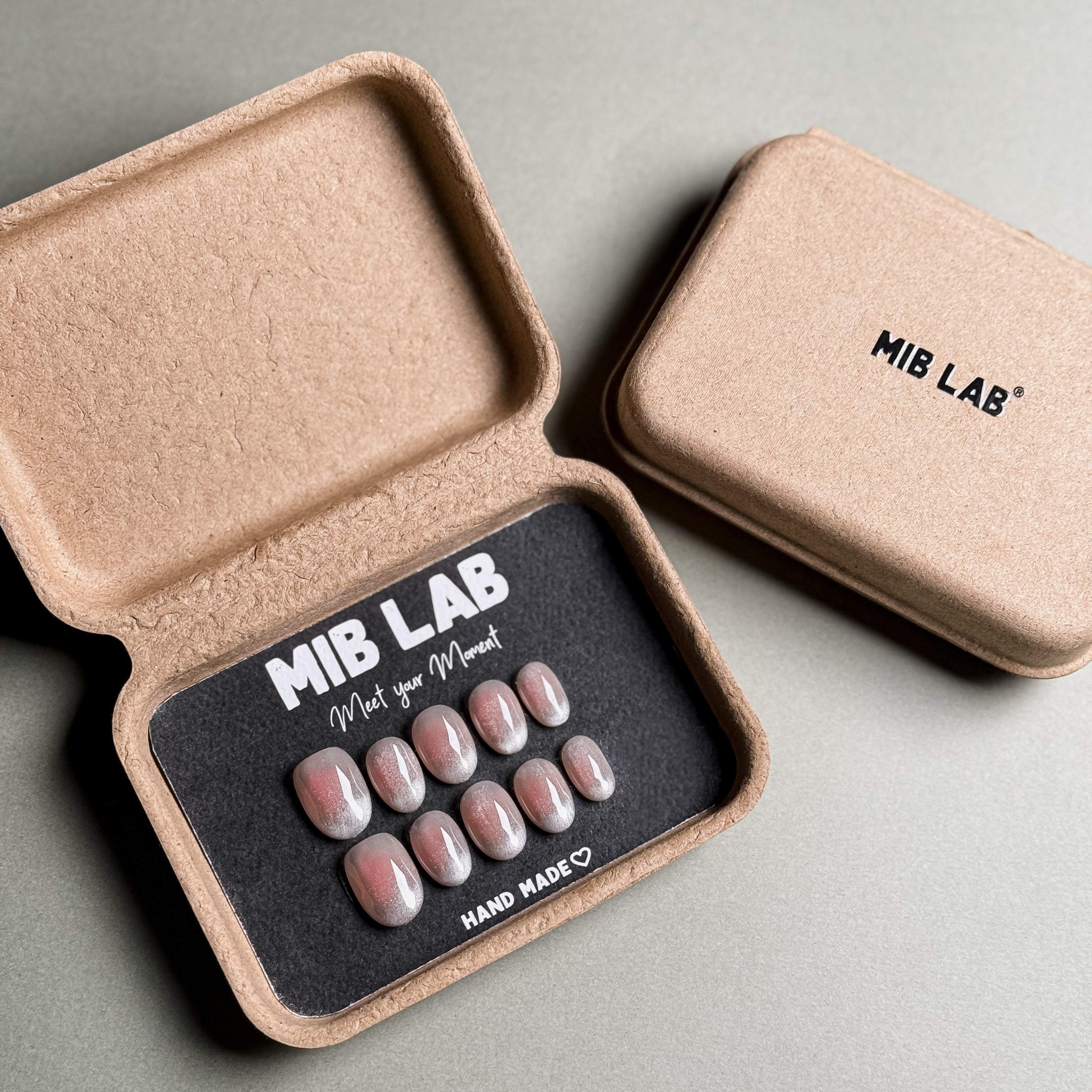 MIBLAB brand silver glitter press-on nails set featuring a dazzling shimmer effect, packaged in an eco-friendly recycled paper box with the brand name "MIB LAB" and the slogan "Meet your Moment" displayed, along with the "HAND MADE ♡" inscription, presented against a neutral gray background, showcasing short nails design. These fake nails offer a quick and easy solution for achieving a glamorous look, suitable for party nails or holiday nails.