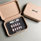 MIBLAB brand silver glitter press-on nails set featuring a dazzling shimmer effect, packaged in an eco-friendly recycled paper box with the brand name "MIB LAB" and the slogan "Meet your Moment" displayed, along with the "HAND MADE ♡" inscription, presented against a neutral gray background, showcasing short nails design. These fake nails offer a quick and easy solution for achieving a glamorous look, suitable for party nails or holiday nails.
