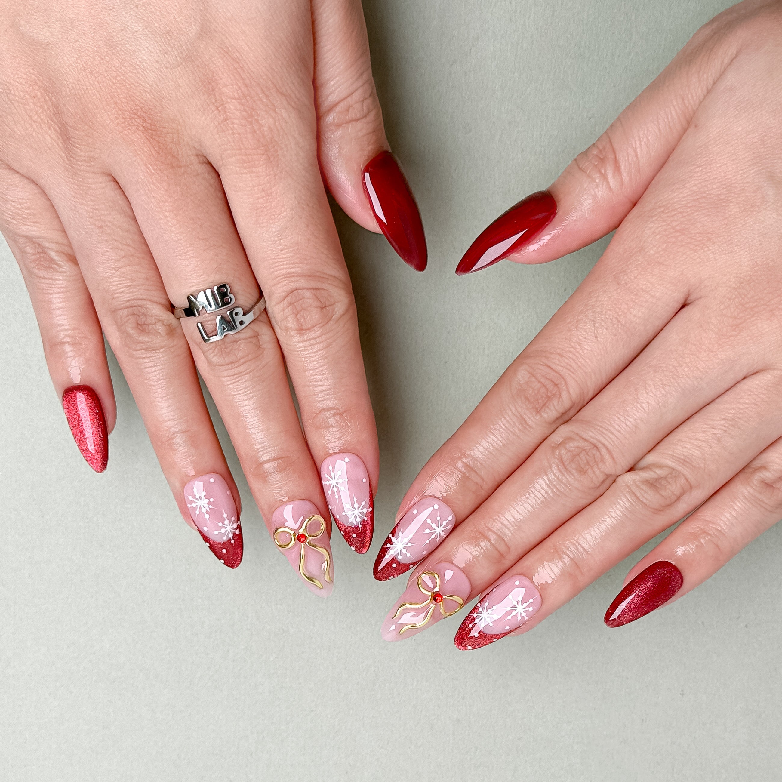 Hands featuring MIBLAB Last Christmas press-on nails in shiny red and nude pink with gold embellishments, luxury reusable manicure from Geneva boutique.