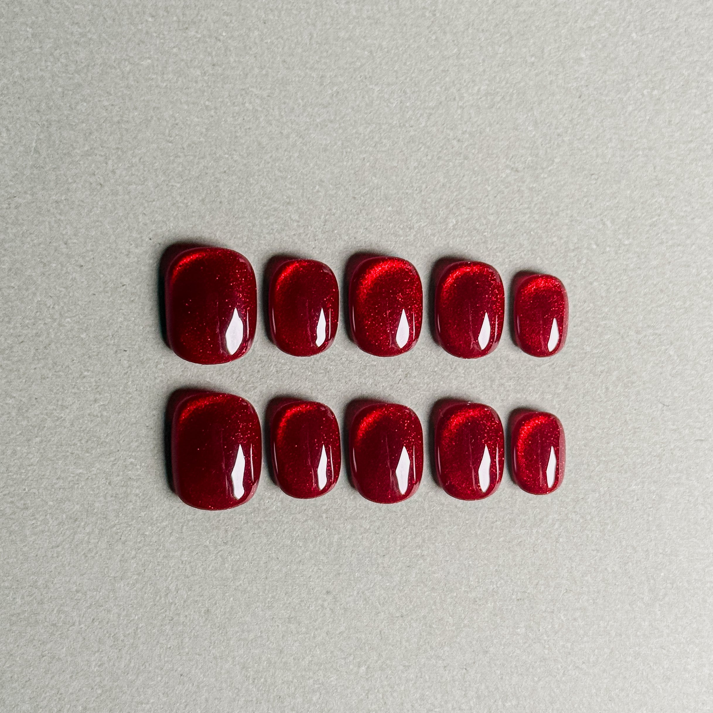 A set of "Echo" red glittery press - on nails with a glossy finish, arranged in two rows for a complete nail set, suitable for festive holiday nail art designs.