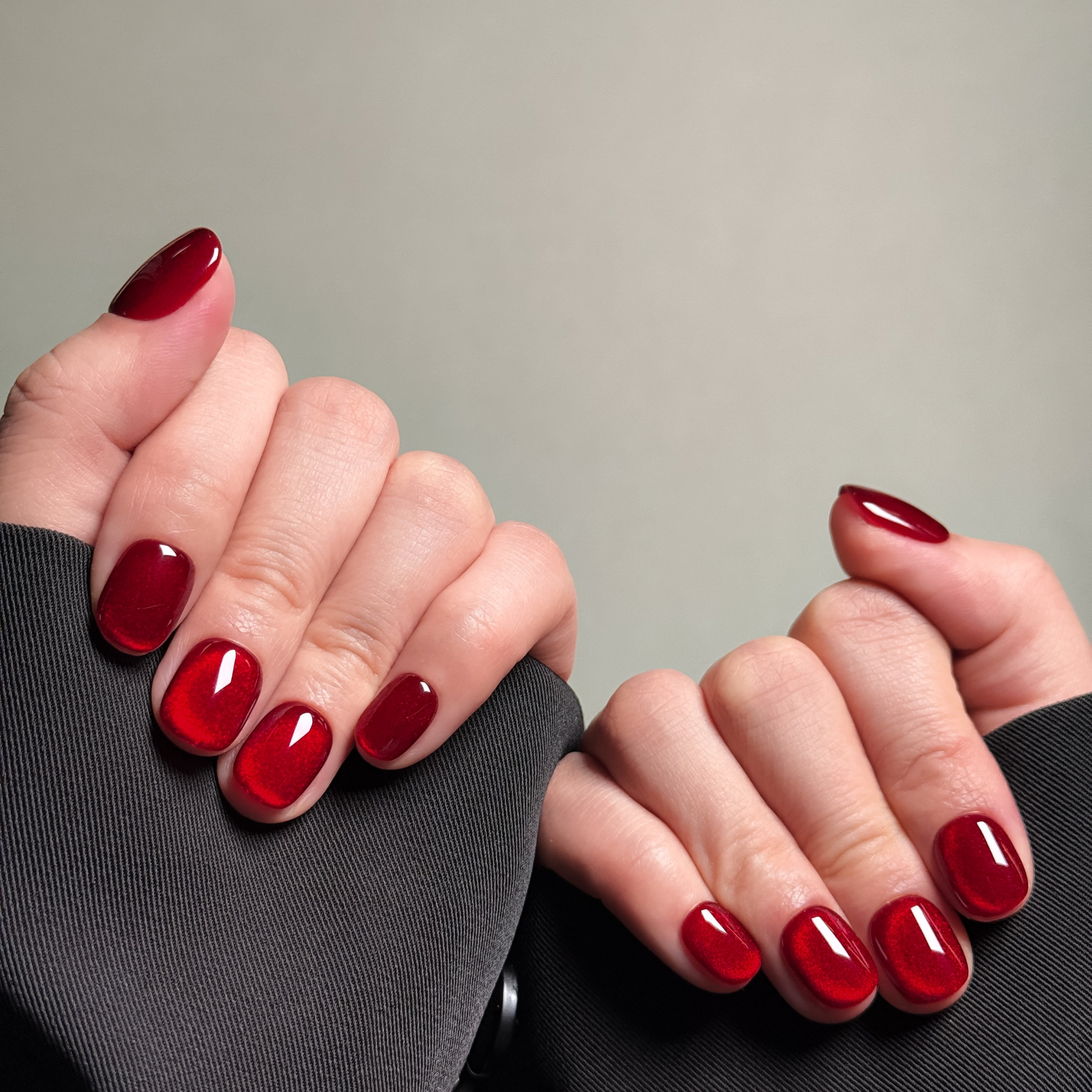 Close-up shot of hands wearing MIBLAB's red press-on nails featuring a high-gloss finish, presented against a neutral gray background and a dark fabric texture, highlighting the vibrant color and polished look on both short and medium nail lengths, showcasing short nails design. These fake nails offer a quick and easy solution for achieving a bold and glamorous look, suitable for party nails or holiday nails.