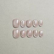 Two rows of MIBLAB's nude cat eye press-on nails, featuring a mesmerizing shimmering effect with a subtle nude hue, arranged against a neutral gray background to highlight the unique texture and depth of the polish, with a gradient of sizes from large to small for a perfect fit, showcasing short nails design. These fake nails offer a quick and easy solution for achieving a natural looking nails effect with a touch of glamour, suitable for everyday nails or minimalist nails.