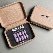A set of Handmade press on nails with a solid lavender color, presented in eco-friendly packaging. These Minimalist nails offer a clean and sophisticated look, perfect for Everyday nails and professional settings. The box, labeled "MIB LAB" and "Meet Your Moment", highlights the brand's dedication to creating timeless Nail art designs. Ideal for those seeking Reusable fake nails that are both stylish and sustainable.