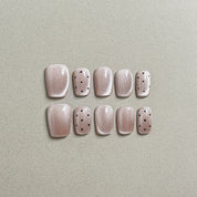 Two rows of MIBLAB's light pink press-on toenails with subtle black polka dot designs, featuring a soft shimmer and a glossy finish, arranged against a neutral gray background to highlight the delicate pattern and elegant color palette, with a gradient of sizes from large to small for a perfect fit.