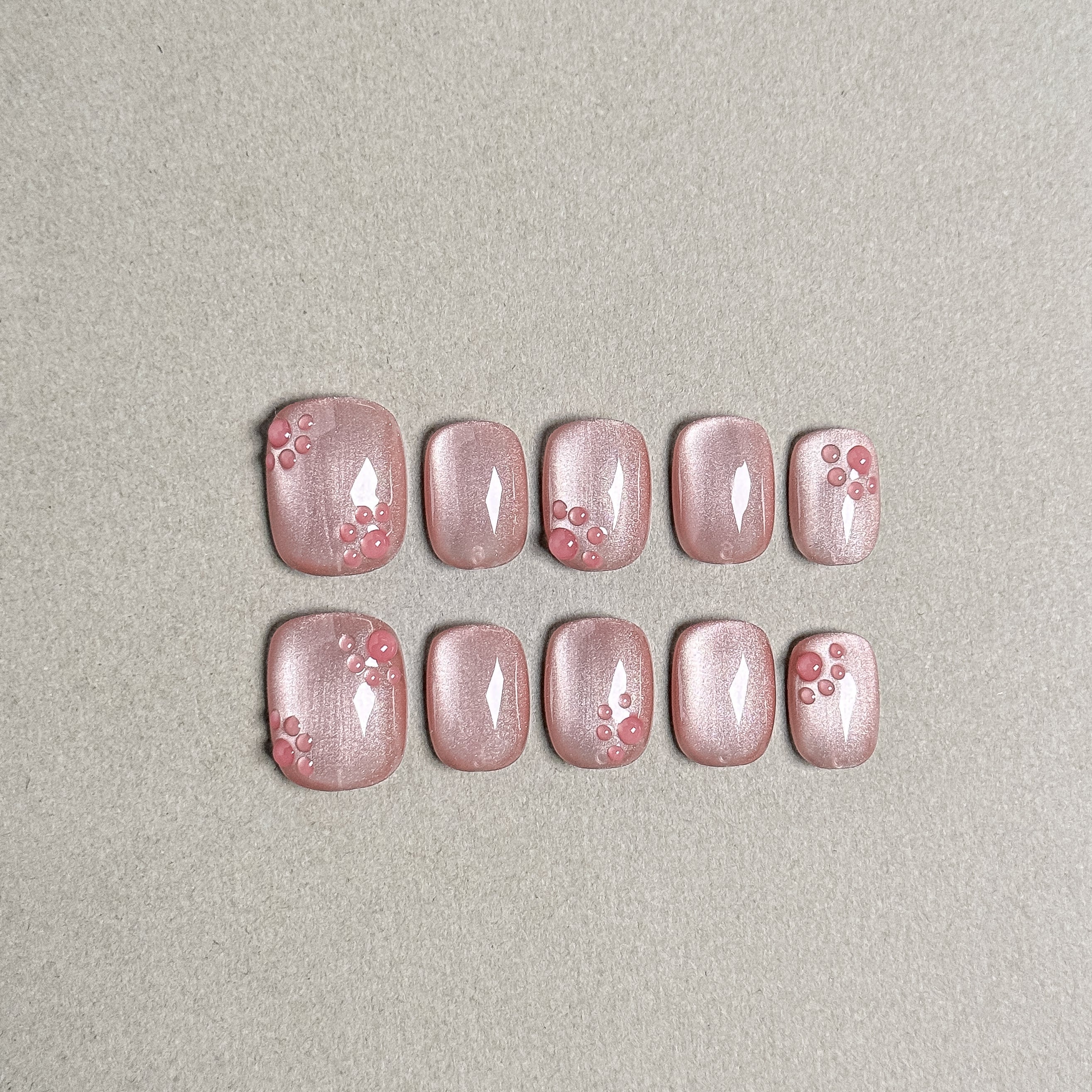 Two rows of MIBLAB's light pink press-on toenails with delicate pink floral designs, featuring a subtle shimmer and a glossy finish, arranged against a neutral gray background to highlight the intricate details and soft color palette, with a gradient of sizes from large to small for a perfect fit.