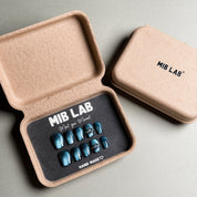 A set of Handmade press on nails with a deep teal finish and silver ring accents, presented in eco-friendly packaging. These Luxury press on nails offer a bold and unique look, perfect for Party nails or special occasions. The box, labeled "MIB LAB" and "Meet Your Moment", highlights the brand's dedication to creating memorable Nail art designs. Ideal for those seeking Reusable fake nails that combine style and sustainability.