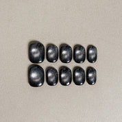 Two rows of MIBLAB's dark gel polish cat eye press-on toenails, showcasing a mesmerizing deep blue-black hue with a shimmering cat eye effect, arranged against a neutral gray background to highlight the unique texture and depth of the polish, with a gradient of sizes from large to small for a perfect fit.