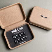 MIBLAB brand press-on toenail set featuring dark gel polish cat eye toenails with a shimmering blue-black cat eye effect, packaged in an eco-friendly recycled paper box with the brand name "MIB LAB" and the slogan "Meet your Moment" displayed, along with the "HAND MADE ♡" inscription, presented against a neutral gray background.