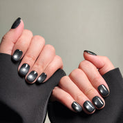 Close-up shot of hands wearing MIBLAB's silver gel polish cat eye press-on nails, showcasing a mesmerizing metallic silver hue with a shimmering cat eye effect, presented against a neutral gray background and a black fabric texture, highlighting the unique texture and depth of the polish on both short and long nail shapes.