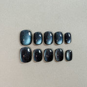 Two rows of MIBLAB's dark gel polish cat eye press-on toenails, showcasing a mesmerizing deep blue-black hue with a shimmering cat eye effect, arranged against a neutral gray background to highlight the unique texture and depth of the polish, with a gradient of sizes from large to small for a perfect fit.