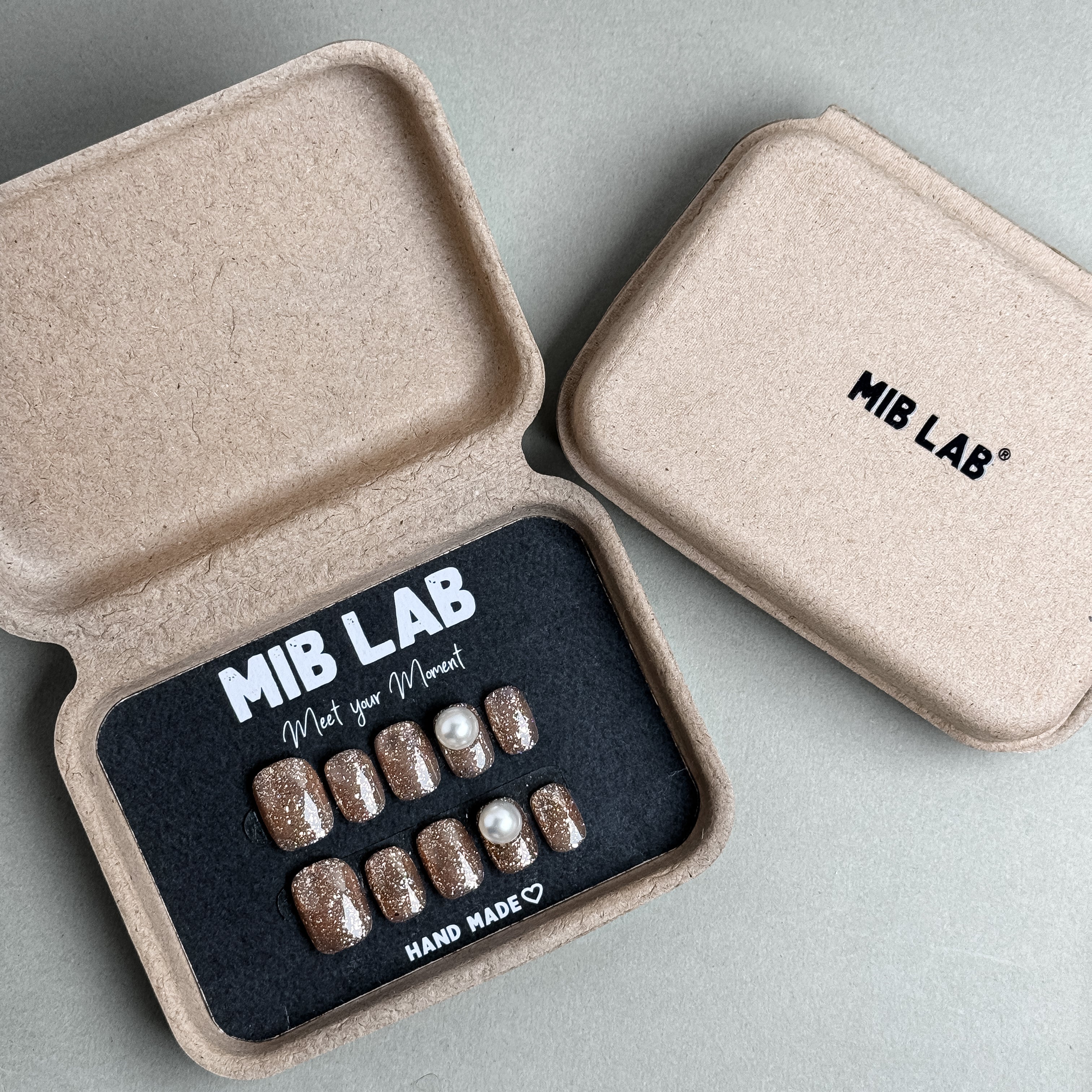 MIBLAB Me Time press-on nail set in soft beige glitter finish with pearl details, packaged for boutique display in Geneva.