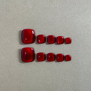 Two rows of MIBLAB's vibrant red press-on toenails, featuring a glossy, gem-like finish reminiscent of rubies, arranged against a neutral gray background, showcasing a gradient of sizes from large to small for a perfect fit, highlighting the luxurious and polished look of the pedicure set.