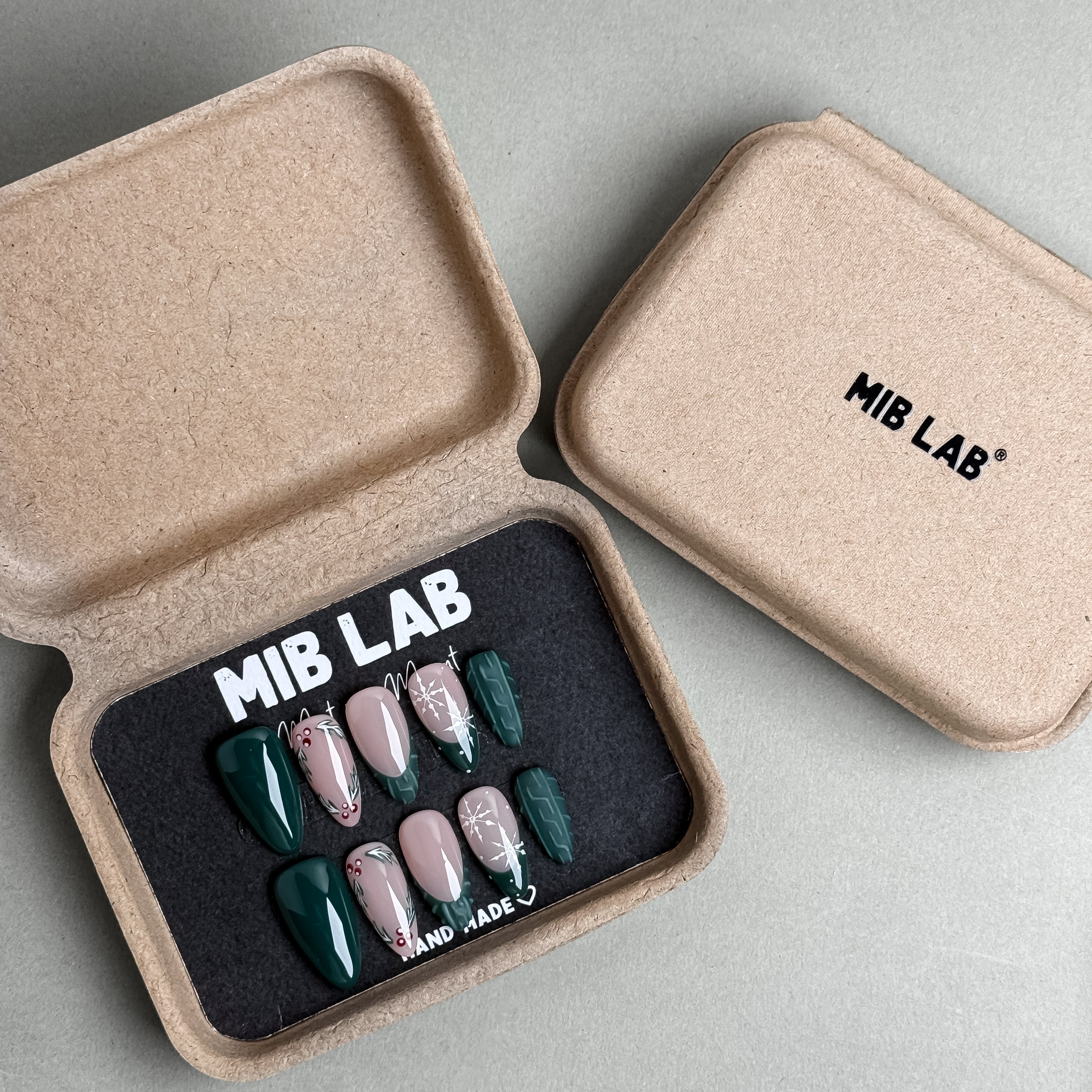 MIBLAB Under My Tree press-on nail set in forest green and nude tones with elegant botanical patterns, packaged for boutique display in Geneva.