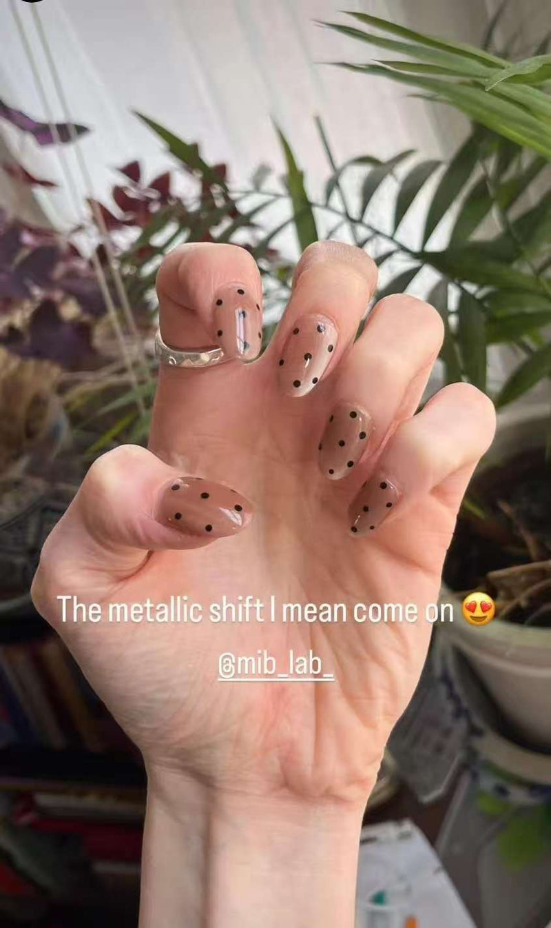 Close-up of reusable press-on nails with nude metallic polish and black dot nail art design by MIB LAB