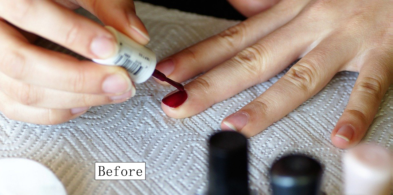 A "Before" image showing a close-up of a woman applying deep red nail polish to her fingernails. The nail polish bottle is visible, and the background features a textured paper towel with blurred outlines of other nail polish bottles. This image captures the initial step of a DIY manicure process.