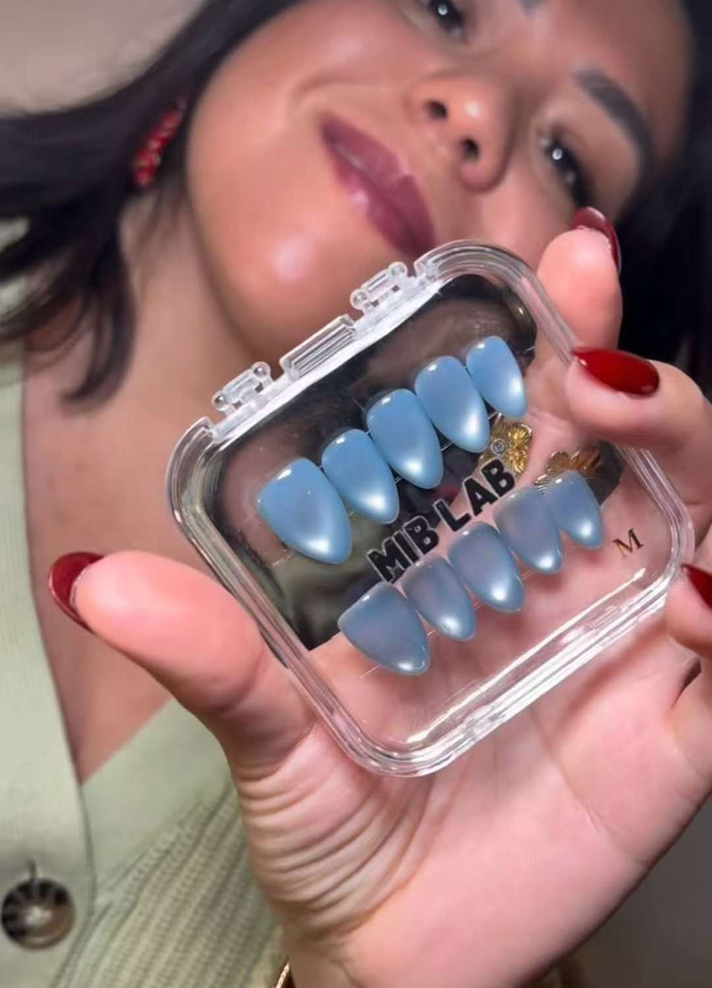 Gros plan : une cliente tient une boîte MIB LAB avec des press-on nails bleu pastel en forme amande, ses ongles rouges visibles au premier plan.
