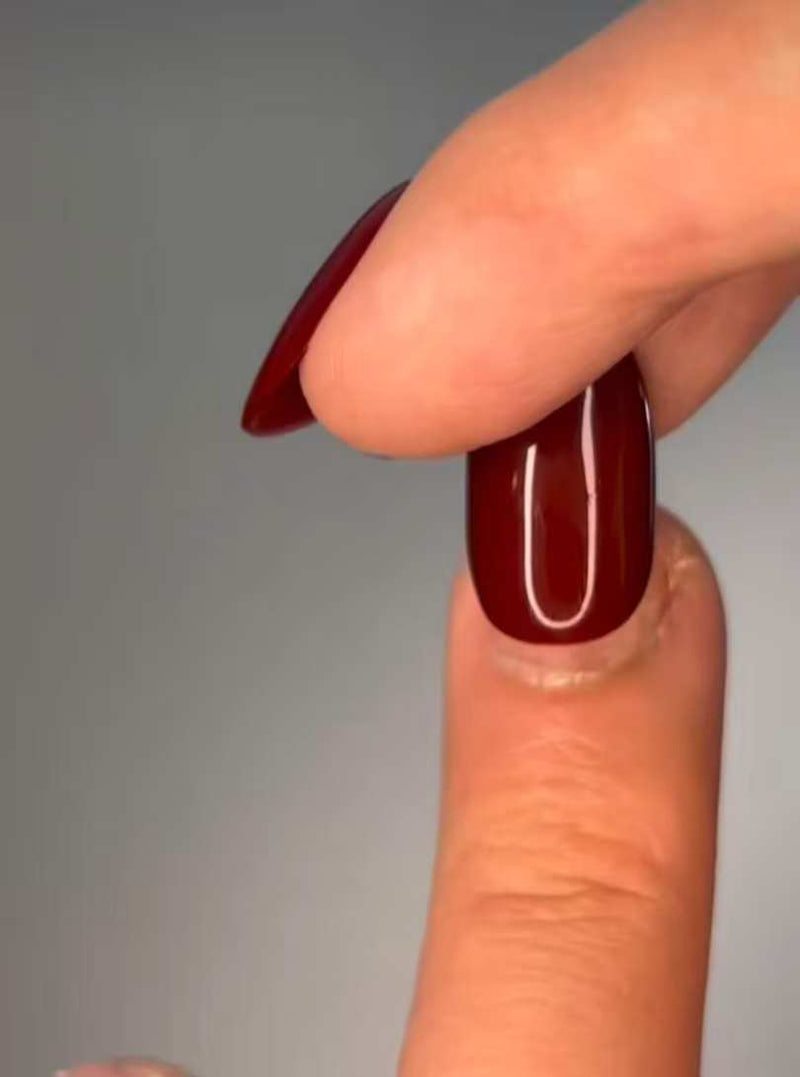 Gros plan : pose d’un faux ongle rouge bordeaux brillant sur un doigt, finition lisse effet salon.