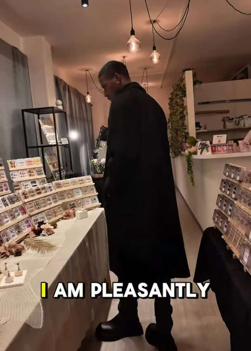 Un client dans une boutique parcourt un présentoir de press-on nails (faux ongles), éclairage chaleureux et étagères de produits autour.