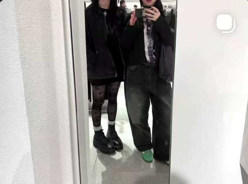 Photo miroir : deux personnes en tenue noire dans une cabine d’essayage, mains visibles avec manucure press-on.
