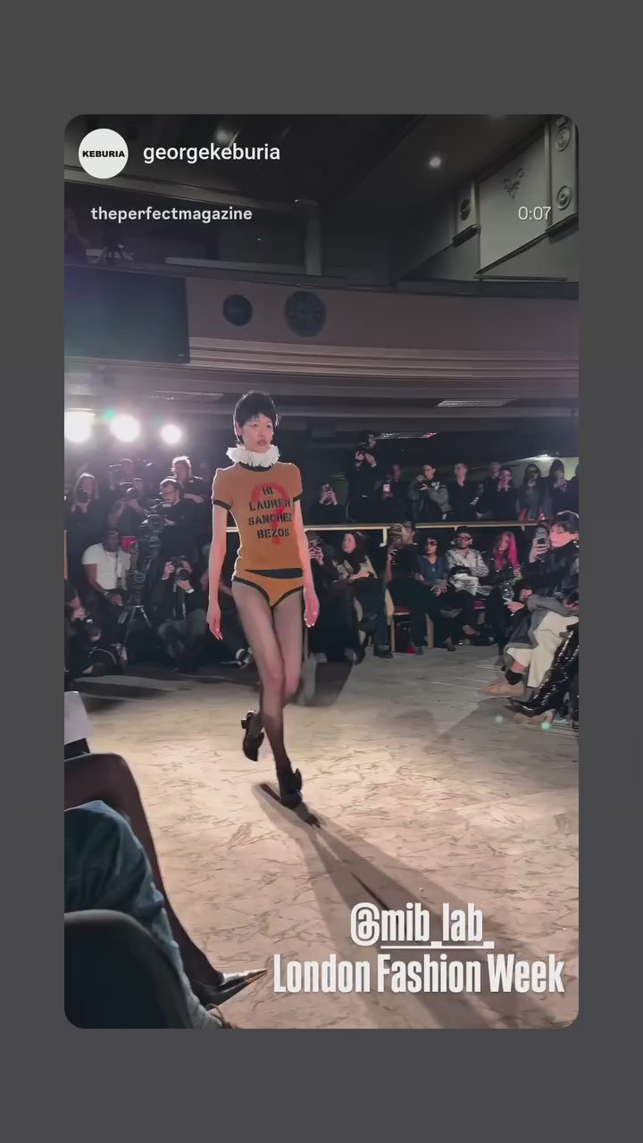 Défilé London Fashion Week : un mannequin marche sur le runway lors du show George Keburia, public assis de chaque côté, tag @mib_lab.
